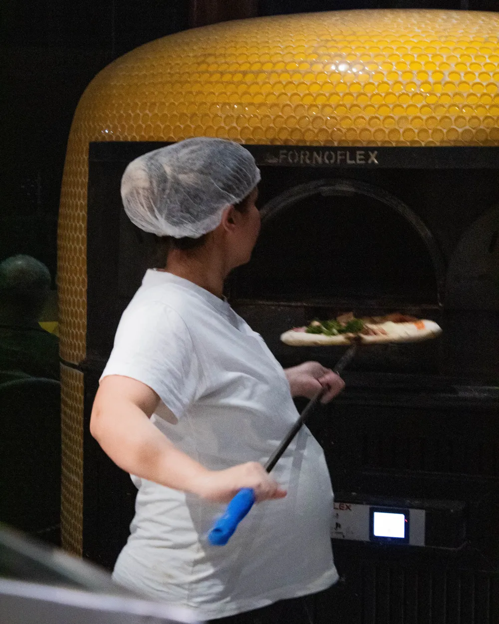 Pizzaiola da D'Angelo levando a pizza ao forno de cúpula amarela