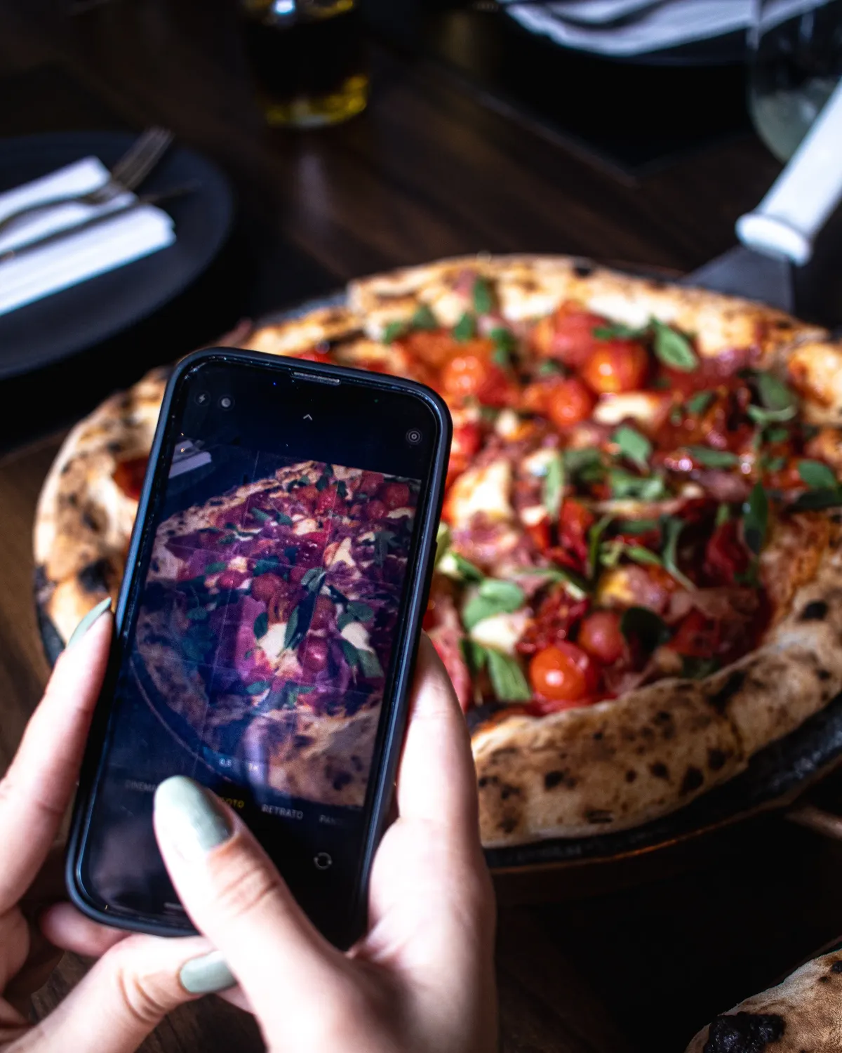 Pizza de borda alta com tomatinhos e manjericão, fotografada na mesa do salão da D'Angelo