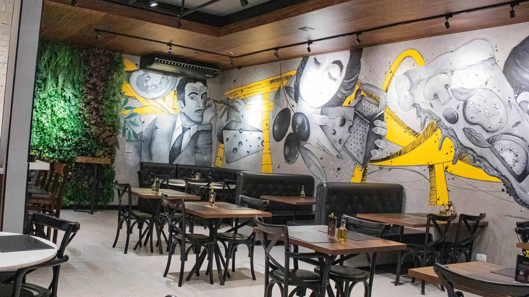 Salão da D'Angelo com mural em preto, branco e amarelo, mesas de madeira e jardim vertical